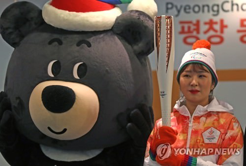 资料图片：展示平昌冬残奥会圣火火炬与火炬手服装的模特站在吉祥物旁边。（韩联社）