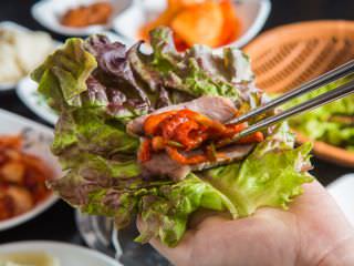 将白切肉、特制包肉泡菜放在生菜上，卷起来食用